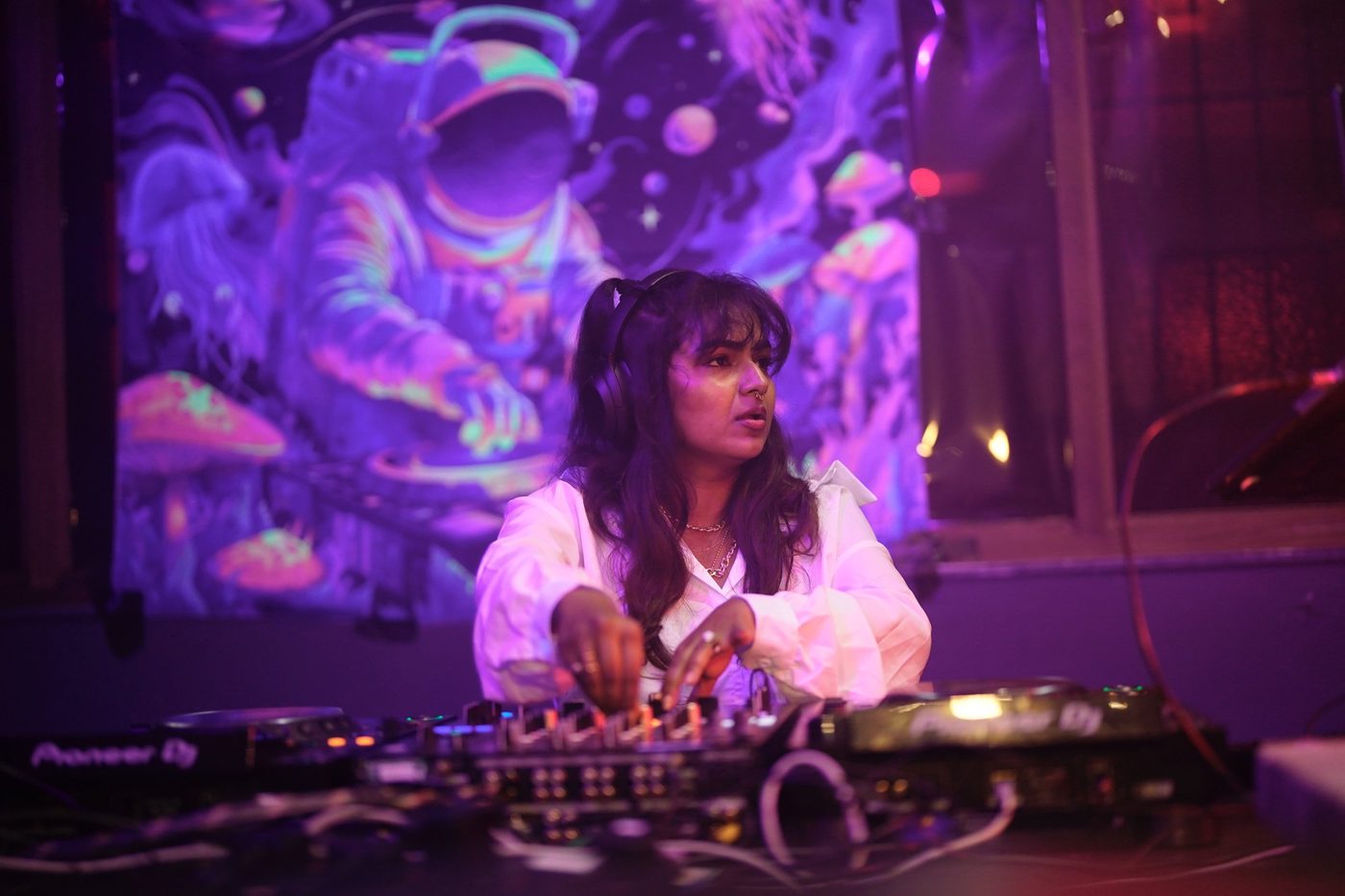 JuLix at the decks in front of a purple astronaut mural