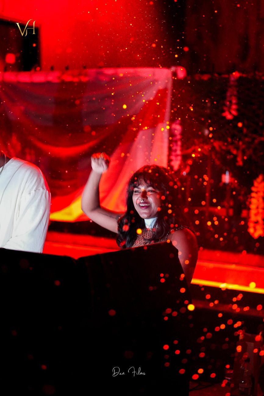 JuLix with her arm raised in red stage light and sparks
